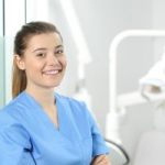 Portrait of a young female doctor wearing a blue coat posing in a dentist office with medical equipment in the background